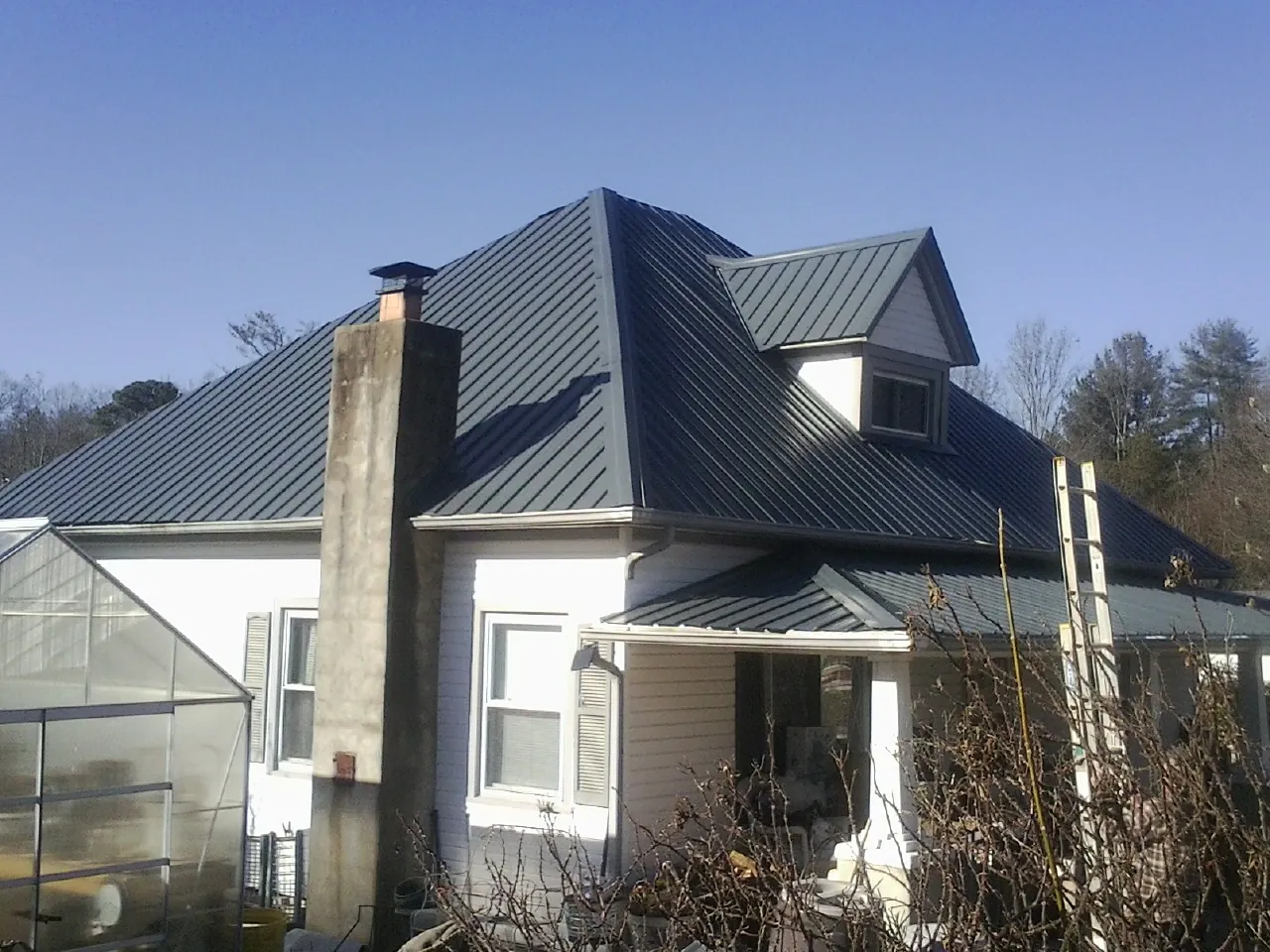 Dark blue standing seam metal roof on a white farmhouse with dormer in Manley