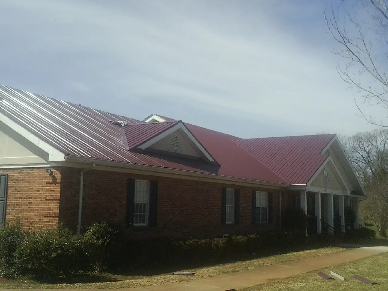 Red metal roof with gabled entries on a long brick building, from a Hail Damage Roof Repair job in Manley