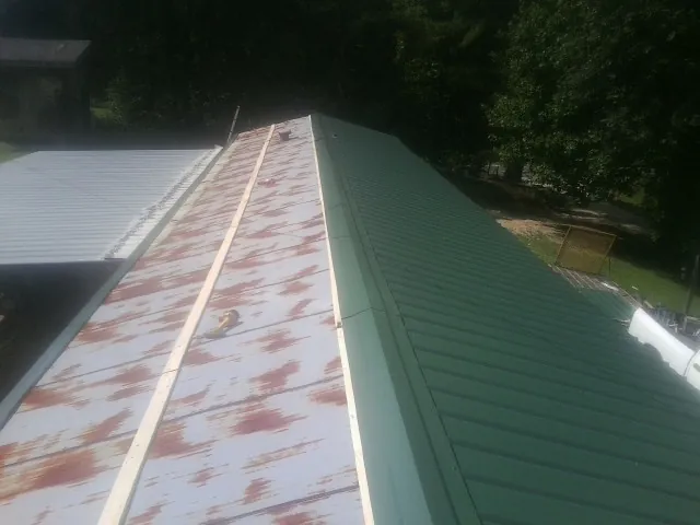 Old rusted panels beside newly installed green metal roofing — Wind Damage Roof Repair by Roofing Brothers in Manley