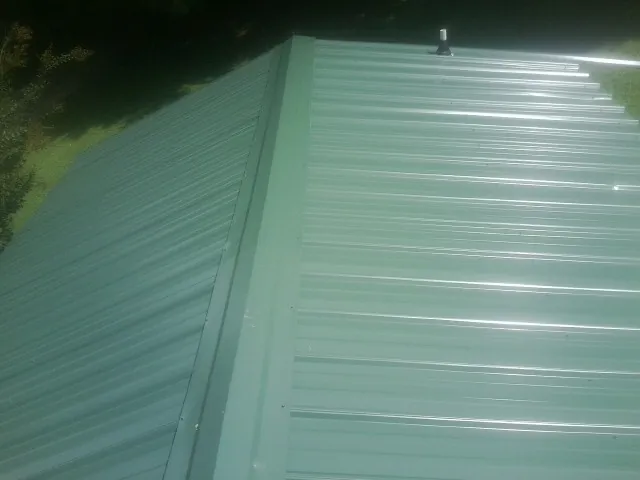 New green metal panels meeting at the ridge of a roof — Flat Roof Repair work by our crew in Manley