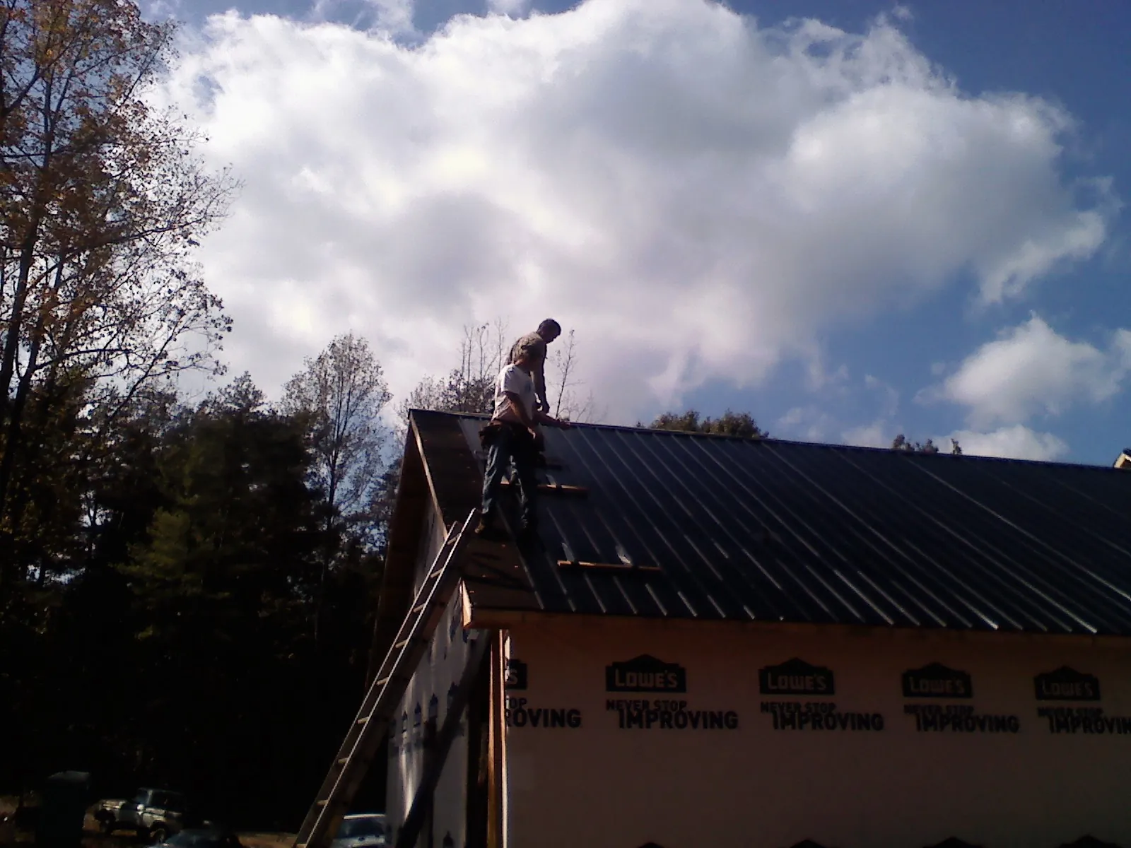 Roofer fastening dark metal panels high against a cloudy sky, from a Roof Inspection job in Manley