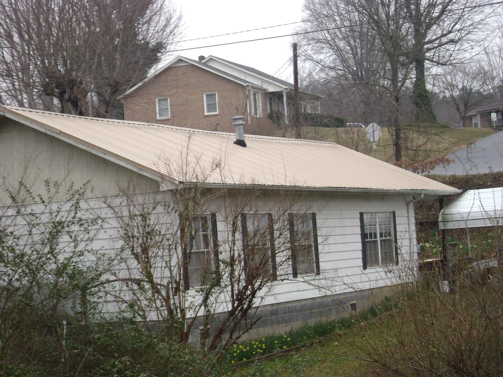 Tan metal roof on a white sided house set into a hillside — Commercial Roofing by Roofing Brothers in Manley
