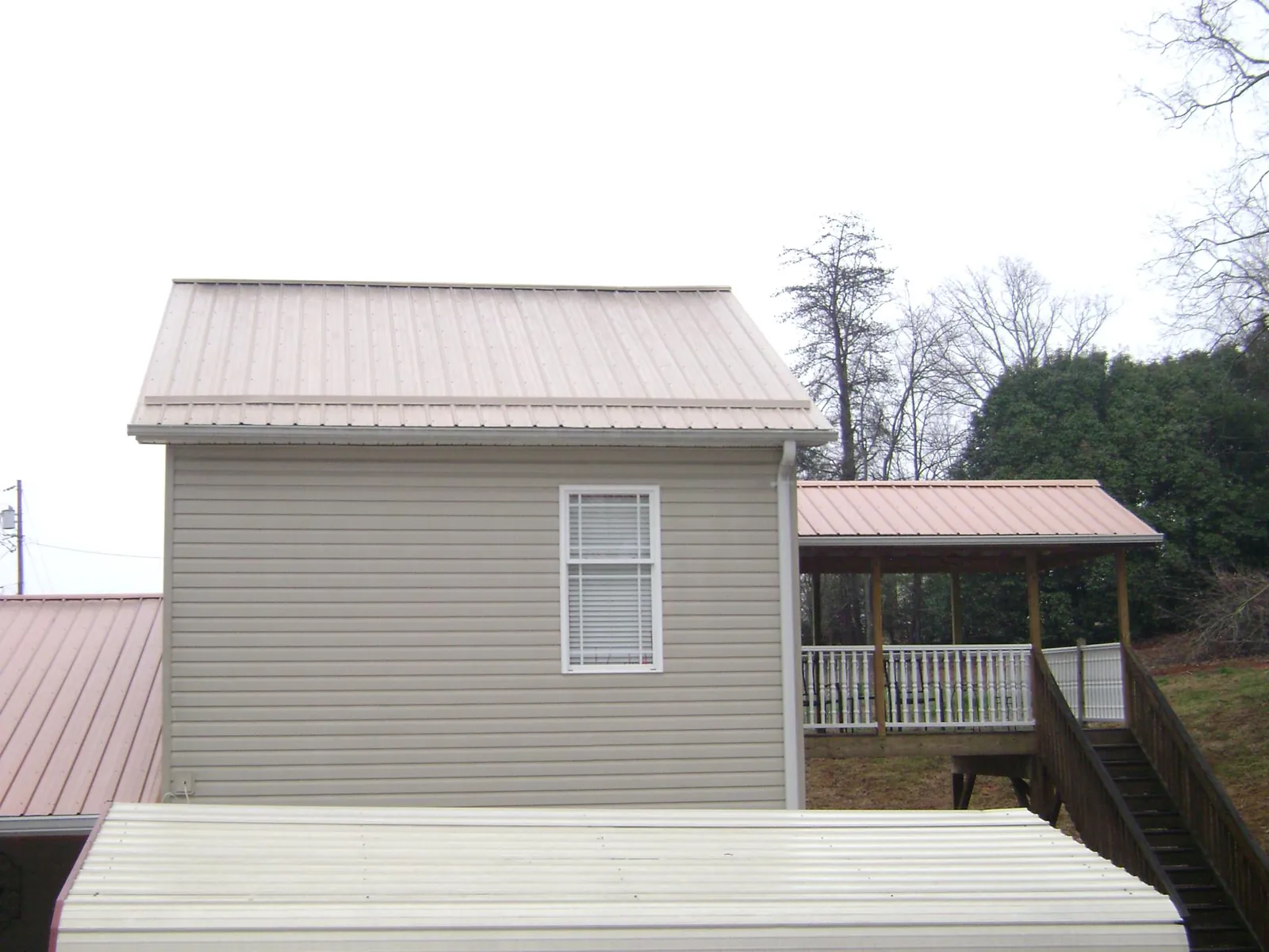 Tan metal roofs on a two story addition and attached porch, from a Roof Replacement job in Manley